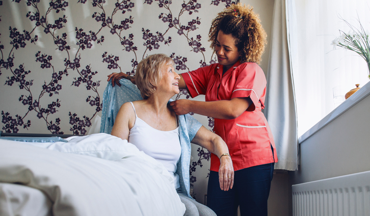 Female nurse dressing a senior female patient sitting on bed